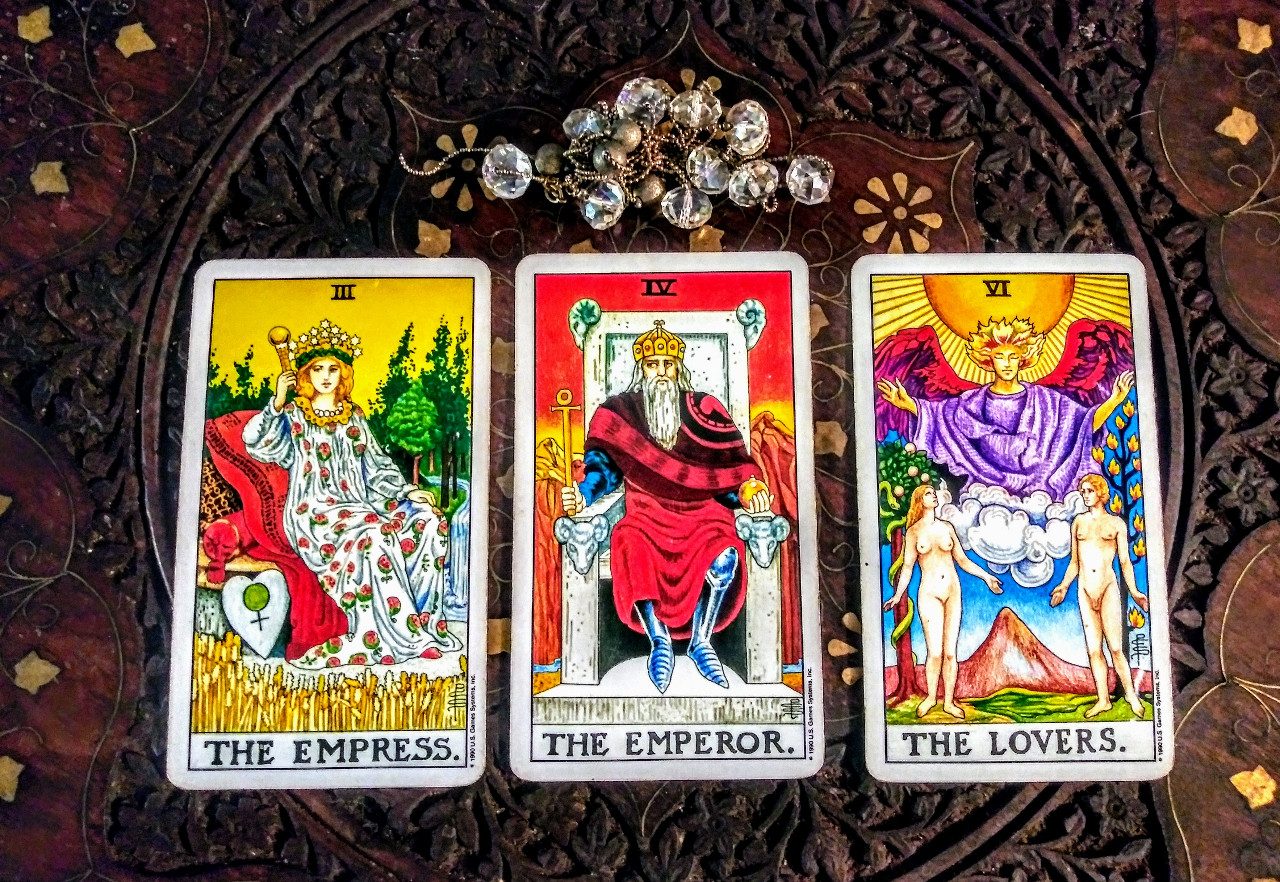 A three-card tarot spread laid out on a cloth surface, representing past, present, and future for love manifestation
