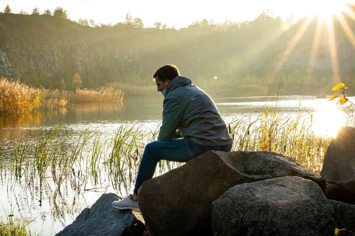 A figure sitting alone by still water as the sun rises, the dawn after the worst of the Ten of Swords