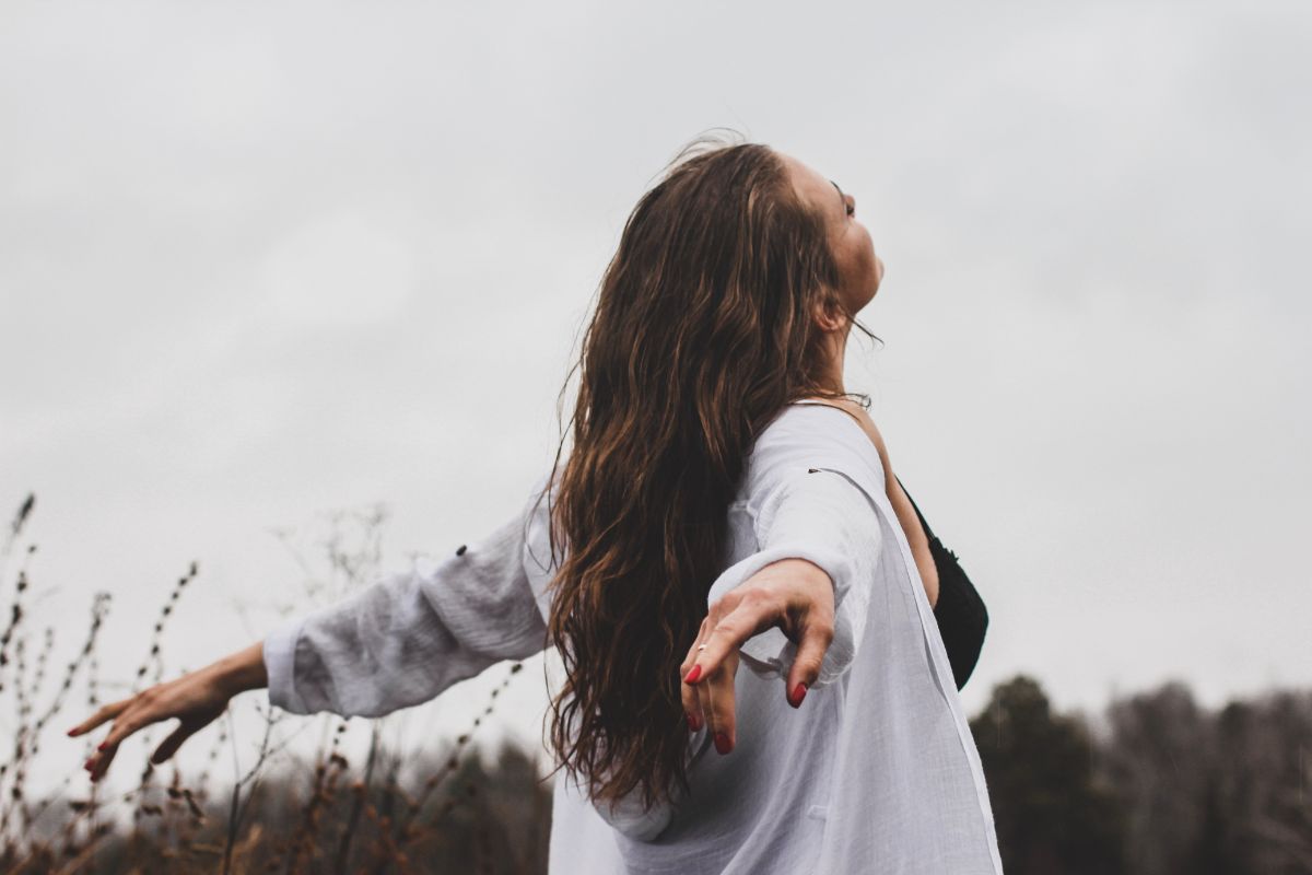 A woman standing in an open field with her arms spread wide and her face lifted to the sky, an image of emotional release and an open heart