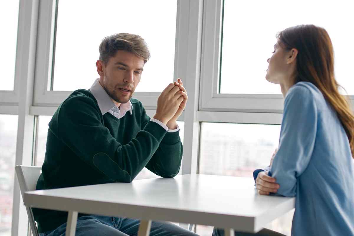 A man sitting with a closed expression, his gaze averted as his partner tries to make eye contact